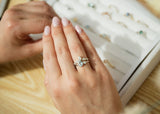 Aquamarine and diamond engagement ring on hand next to ring tray of engagement rings