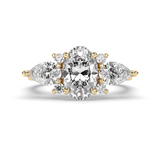 A yellow gold three-stone diamond ring featuring a large oval center diamond flanked by two smaller round diamonds, with pear-cut side diamonds, set against a clean white background.