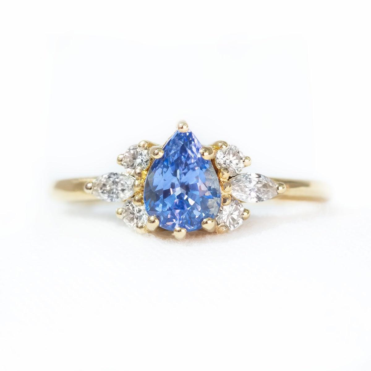 Pear blue sapphire cluster ring with round and marquise shape white diamonds in 18K yellow gold on white background by Amy Jennifer Jewellery