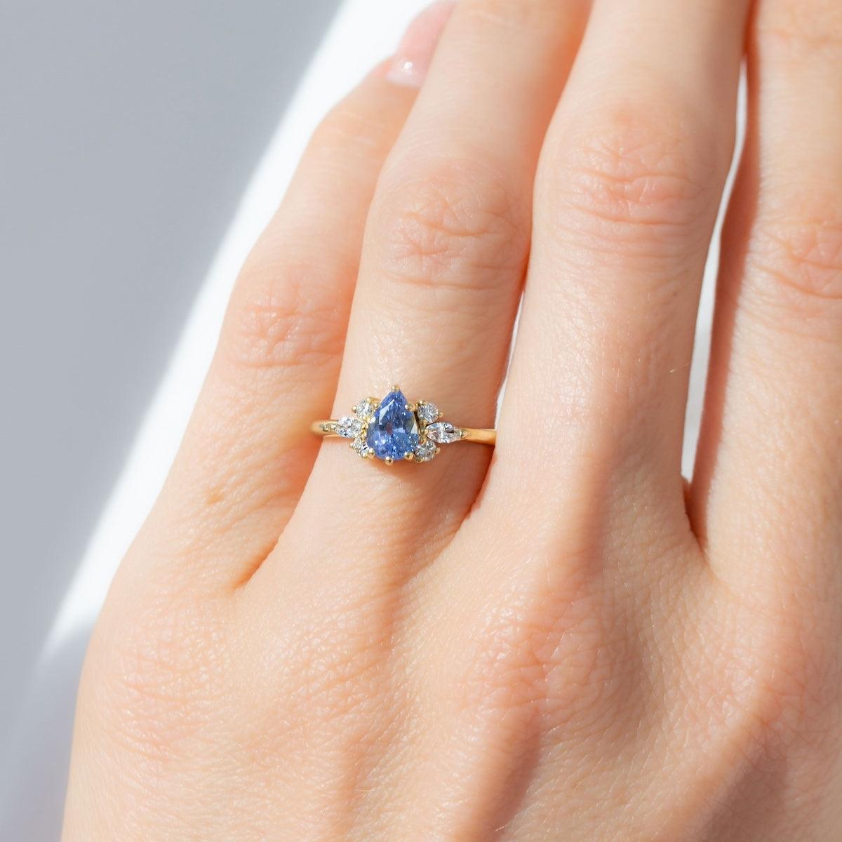 Pear blue sapphire cluster ring with round and marquise shape white diamonds in 18K yellow gold on hand by Amy Jennifer Jewellery