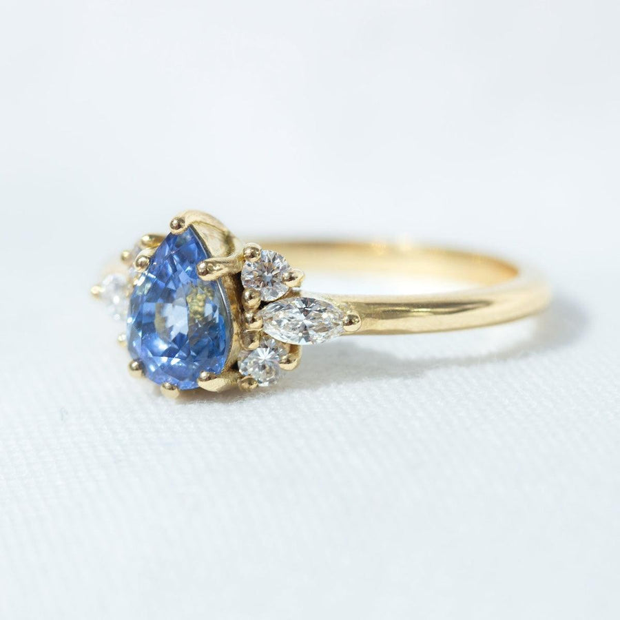 Pear blue sapphire cluster ring with round and marquise shape white diamonds in 18K yellow gold on white background by Amy Jennifer Jewellery