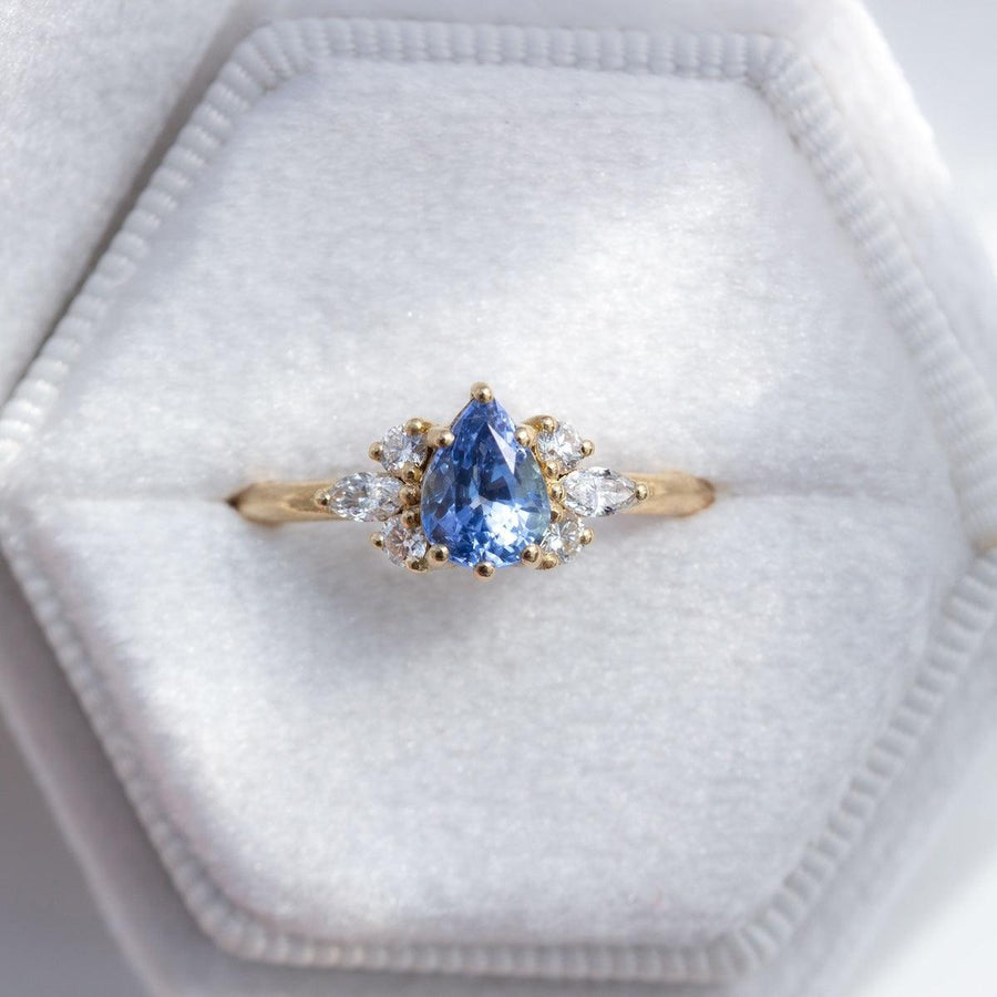 Pear blue sapphire cluster ring with round and marquise shape white diamonds in 18K yellow gold in whit velvet ring box by Amy Jennifer Jewellery